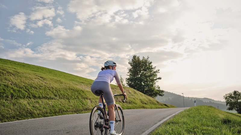 Rennradlerin fährt auf Straße Richtung Horizont Rennradlerin fährt auf Straße Richtung Horizont
